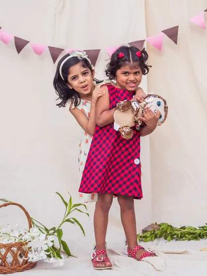 Best friends having fun. One girl wears a simple printed A-line dress while the other is in a playful red and blue checkered design, both perfect for a day of play.