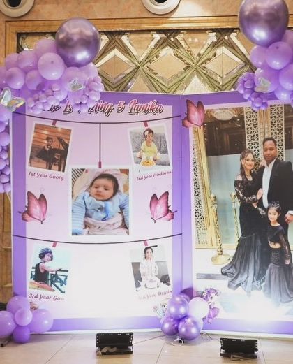 This butterfly-themed birthday features a personalized photo collage backdrop, allowing you to share precious memories with your guests. The setup is framed by purple balloon garlands and wooden 'BABY' blocks.