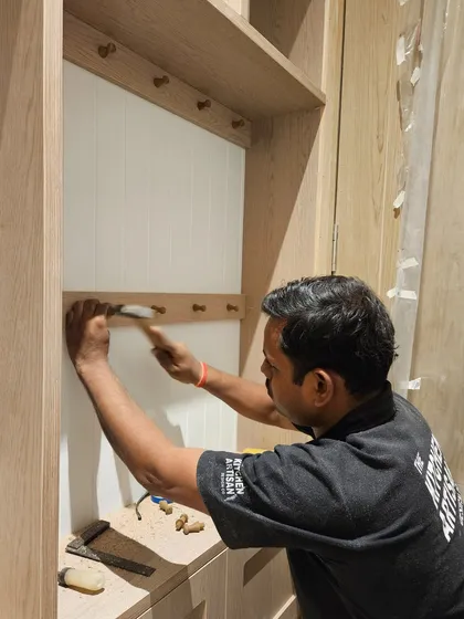 A craftsman at work, carefully installing the wooden pegs on a custom shelving unit. It is this attention to detail and handcrafted quality that defines our work.