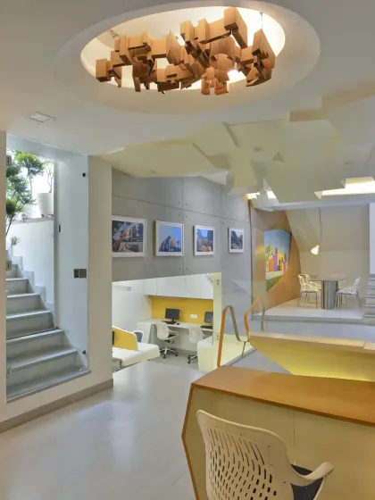 The front section of my studio serves as a gallery, with a glass roof that invites natural light into the basement space. An informal conference area sits on a raised platform, featuring a custom table and an abstract ceiling panel.