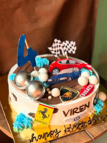 A cake for a little car enthusiast, featuring logos from Ferrari, Lamborghini, and Bugatti. The road on top is made from chocolate, perfect for racing the toy car toppers.