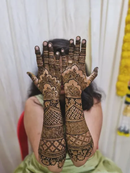 A classic pose hiding the bride's face, putting the focus entirely on the beautiful, intricate mehendi that covers her hands and arms.