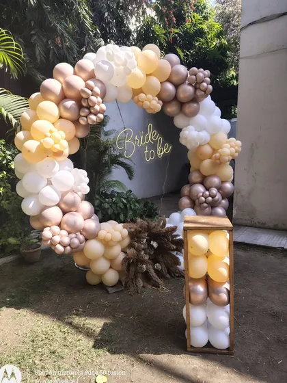 An elegant "Bride to be" party setup outdoors, with a full balloon ring in neutral tones and dried pampas grass for a rustic touch.