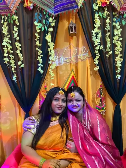 Two friends posing in front of the yellow and black Haldi decoration. The hanging floral strings add a delicate touch to the photos.