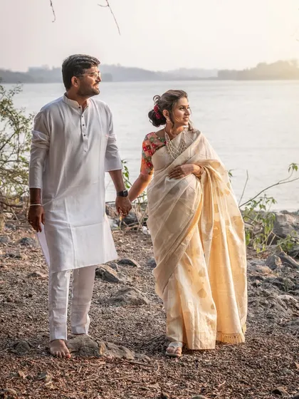 By the water's edge, this couple shares a quiet moment. The simplicity of their white traditional outfits against the serene landscape creates a powerful and soulful image of their bond.