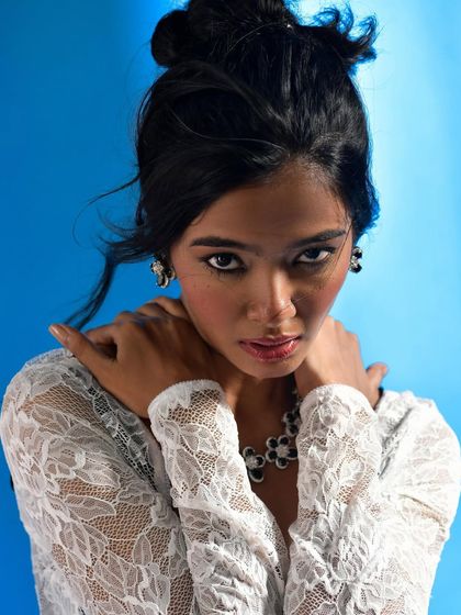 An intense, close-up shot where the model's hands frame her face, drawing attention to the jewelry. Her direct gaze is powerful, making this a strong and captivating image for a campaign.