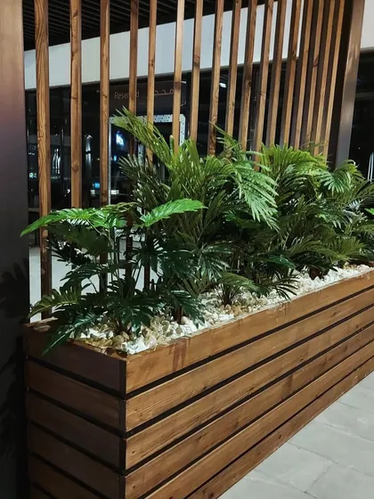 A large wooden planter serves as a natural divider in this open space. Filled with lush ferns, it adds privacy and a biophilic element that complements the wooden slat wall behind it.