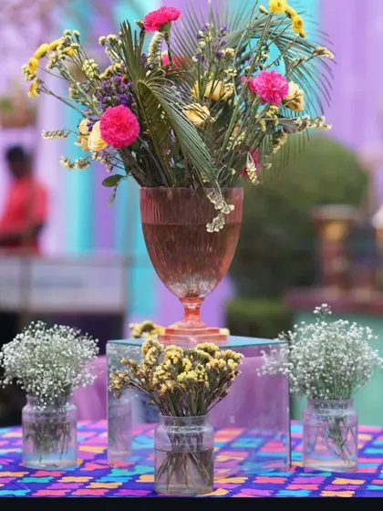 A colorful and eclectic centerpiece arrangement with a variety of flowers and vases, perfect for a vibrant Mehendi or Sangeet.