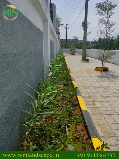 This is a practical landscaping solution for an industrial site in Sriperumbudur. We installed a durable interlocking paver path and a simple planter bed along the compound wall to add a touch of green to the functional space.