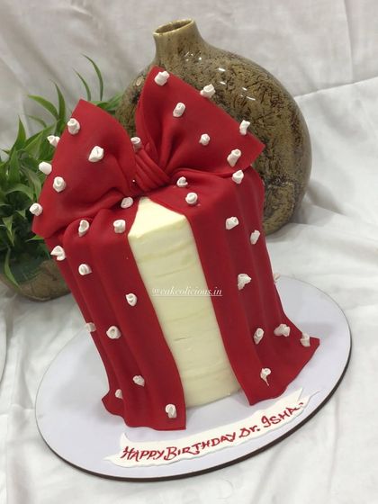 A stylish and elegant cake designed to look like a gift box. This single-tier cake is covered in white ganache and wrapped with a beautiful, hand-sculpted red bow with white floral embossing.