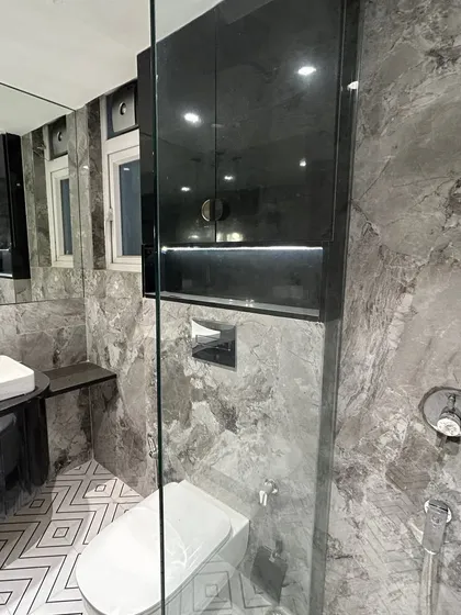 This view shows the clever storage solutions in the bathroom, including a tall cabinet with a black high-gloss finish. The glass shower partition maintains an open feel while delineating the wet area.