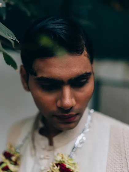A close-up portrait for Sanchit Sharma, framed by leaves. The soft, natural light and downward gaze create a gentle and introspective mood.