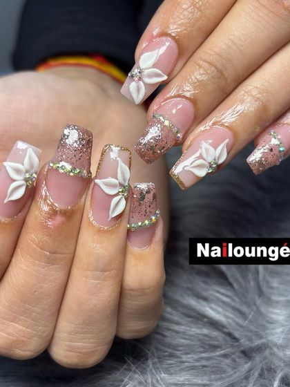 A close-up of a detailed 3D floral design on square nails with a pink glitter base and rhinestone borders.