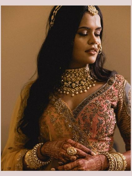 A soft and romantic bridal portrait. The hair is styled in gentle waves and accessorized with a matha patti for a traditional touch.