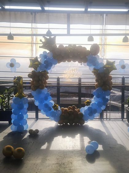A first birthday decoration on a terrace, with a blue and gold balloon ring against the sunset.