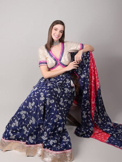 A seated pose showing the beautiful drape of the royal blue lehenga and its contrasting pink and blue dupatta. The outfit is designed for both comfort and style.