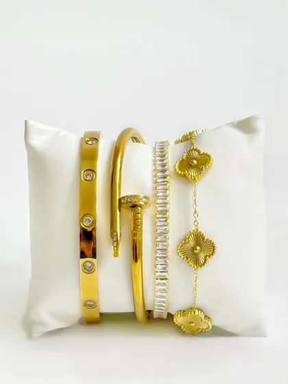 A creative display of gold bracelets on a white cushion. This unique presentation is more engaging than a standard flatlay and works well for social media or website hero images.