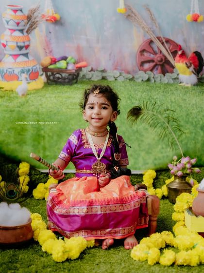 A smiling little Radha sits amidst a colorful Janmashtami setup. Her happy expression and the festive decorations make this a joyful and memorable shot.