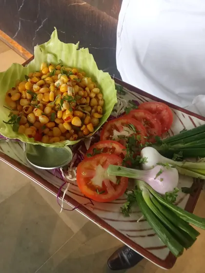 A simple yet flavorful corn chaat served in a lettuce cup. This dish is a light and healthy starter, presented beautifully on a platter with fresh tomato and spring onion garnish.