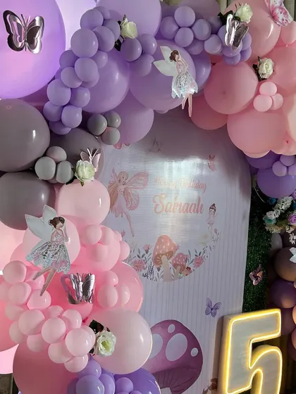 A beautiful shot of the balloon arch from the fairy-themed party, showing the mix of pastel pink, purple, and grey balloons. The arch is adorned with small fairy cutouts and butterfly stickers, adding layers of detail to the design.