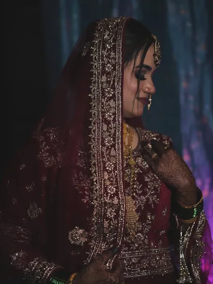 A side profile showcasing the detailed work on the dupatta and the elegant way it frames her face. The makeup is soft yet defined, perfect for a traditional bride.
