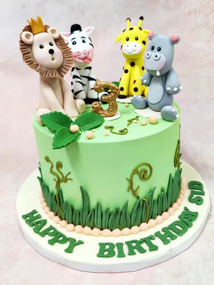 This vibrant green jungle cake is topped with a friendly crew of fondant animals: a crowned lion, a cheeky zebra, a smiling giraffe, and a happy hippo.