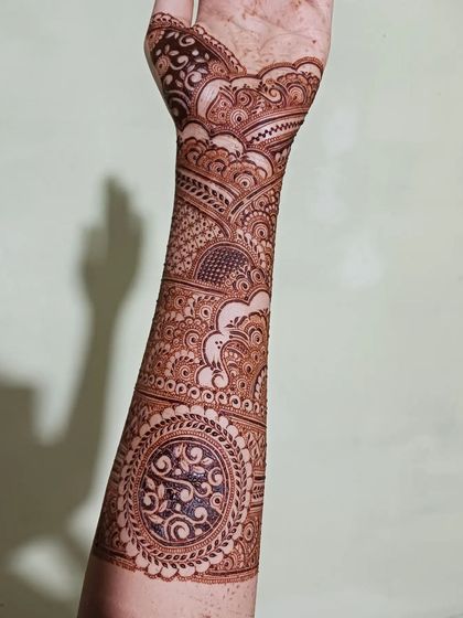 A look at a fully completed bridal henna design with eye-catching mandalas and flowing patterns. The dark fingertips and detailed work create a classic and rich look for any bride.