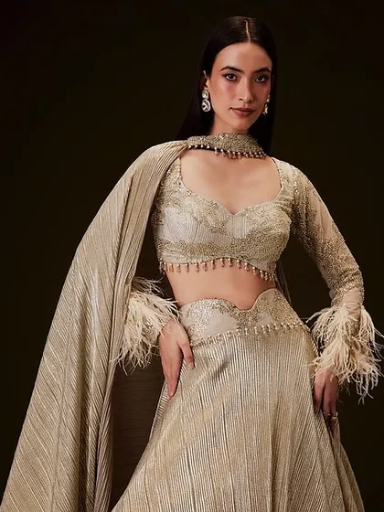 A beautiful look for Kalki Fashion's catalogue. The makeup is soft and neutral, and the hair is styled sleek and straight, ensuring the feathered, gold-toned outfit remains the star of the show.