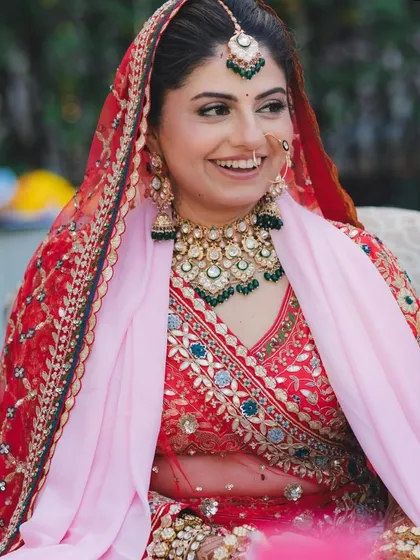 A candid shot of a bride's joyful smile, her face framed by a beautiful dupatta and a sparkling green-beaded Kundan necklace.