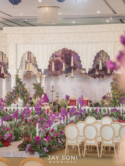 The "Garden of Vows" was a picture of elegance. This wide shot shows the seating arrangement facing a stage filled with beautiful purple and red floral decor and thoughtful details.