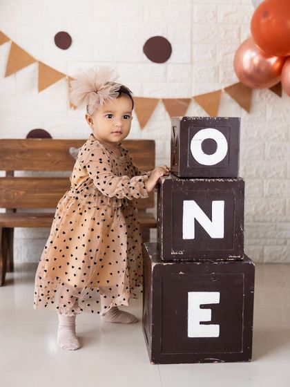 Standing by the 'ONE' blocks, this is a classic first birthday portrait. The polka-dot dress and matching headband complete the adorable look.