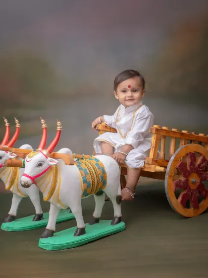 A simple and classic portrait featuring a baby in a white kurta sitting on a decorative bullock cart. This Bail Pola inspired theme is a wonderful way to connect with Maharashtrian agricultural traditions.
