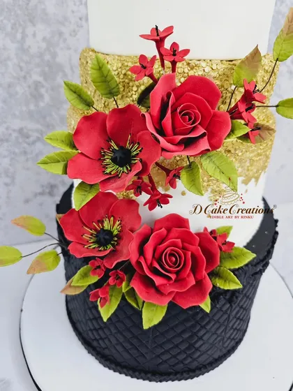 A detailed close-up of the lower tiers, showing the intricate texture on the black fondant and the vibrant, lifelike quality of the red sugar flowers against the edible gold sequins.
