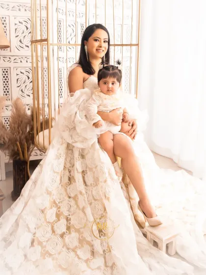 A mother and her baby daughter share a beautiful moment, dressed in elegant, coordinated lace outfits.