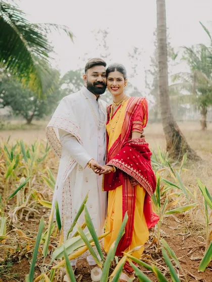 A beautiful portrait of a couple in traditional yellow and red Maharashtrian wedding attire. The natural field setting in Alibag provides a simple, rustic backdrop that makes their colorful outfits and connection stand out.