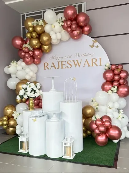 Celebrating a 21st birthday with an elegant touch. This setup features a personalized backdrop, a sophisticated balloon arrangement in rose gold, white, and chrome gold, and a collection of white plinths for displaying cakes and decor pieces.