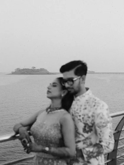 A moody black and white shot of the couple by the sea. The soft focus and dramatic sky create an artistic and romantic portrait that feels like a still from a classic film.