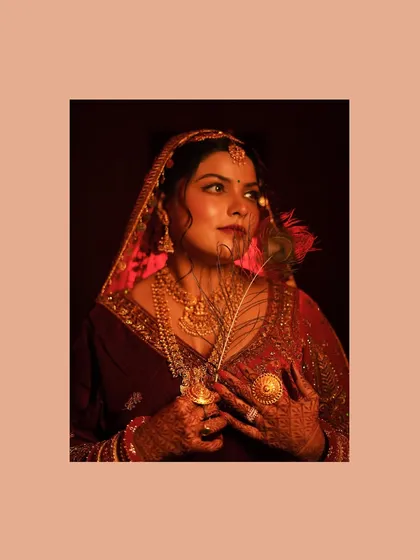 An artistic and moody portrait of a bride in her traditional red wedding lehenga. The use of a peacock feather and veil adds a layer of mystery and timeless beauty.