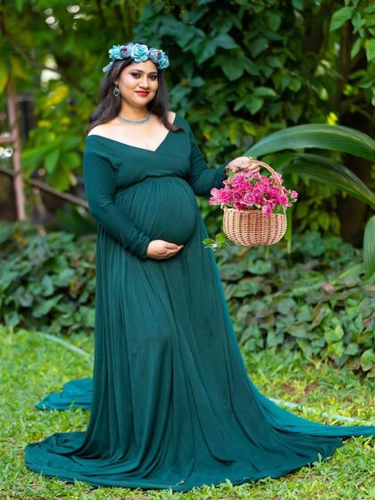 A graceful portrait in a garden. The mom-to-be wears a deep green gown and holds a basket of flowers, looking like a woodland goddess.