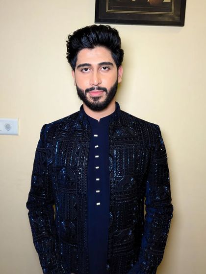 A direct, confident portrait. The makeup enhances his features, providing a flawless skin finish and defining the beard for a sharp look.