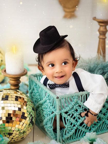 A handsome little gentleman in a hat and bowtie. This shot captures his charming smile and dapper style in a sparkly, festive setting.
