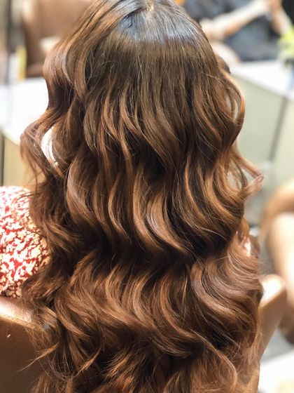 These warm, caramel-toned balayage highlights are styled into soft, beachy waves. This look is perfect for adding warmth and dimension to dark hair, creating a rich and inviting style.