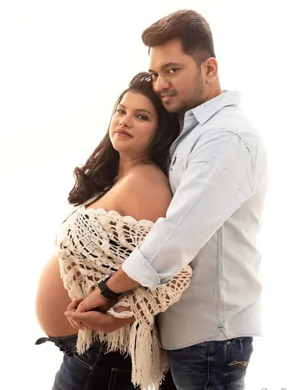 A classic couple maternity portrait against a clean, white background. The focus is all on their loving embrace and the beautiful baby bump.