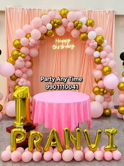 This classic Minnie Mouse decoration for Pranvi's first birthday uses a pink fabric backdrop with a matching balloon arch. I provide foil balloons for the name and age.
