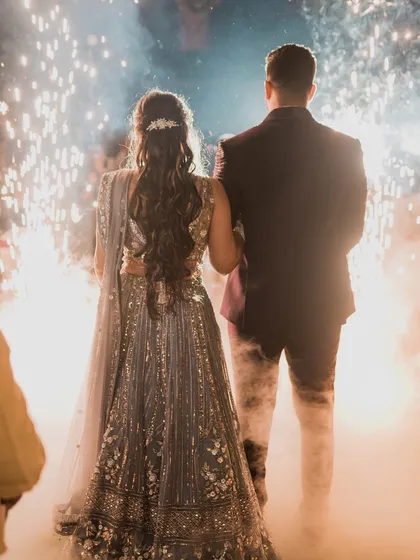 A grand exit or entrance with sparklers. This dramatic shot from the back showcases the bride's beautiful hairstyle and the silhouette of her reception lehenga.