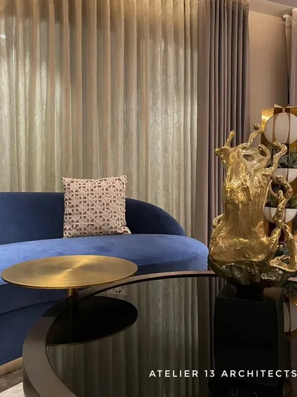 A detail shot of the Shanti Niketan lounge, highlighting the interplay of textures. The deep blue velvet of the sofa contrasts with the cool, reflective surface of the black glass coffee table and a sculptural golden accent piece.
