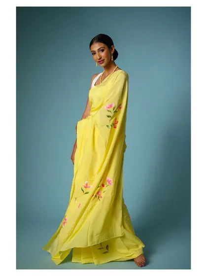 A full-length shot with a slight turn, showing the flow and lightness of the yellow saree's fabric.