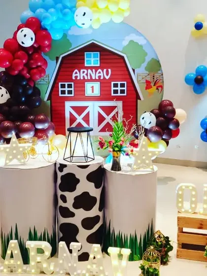I designed this farmyard theme for a first birthday party. The centerpiece is a red barn backdrop with the child's name, surrounded by balloon arrangements and pedestals with cow-print details to match the farm animal theme.