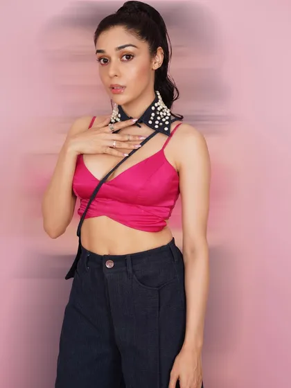 Actress Eisha Singh in a vibrant, high-fashion studio setup. The pink bralette and unique pearl-studded accessory create a trendy and youthful look.