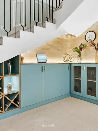 A full view of the under-stair bar, showcasing the custom wine rack and sleek blue cabinets. The modern black metal railing of the staircase adds a graphic element to the design.